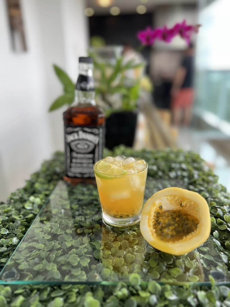 Garrafa de whisky Jack Daniel´s e um copo de coquetel Maracujack ao lado de meio maracujá