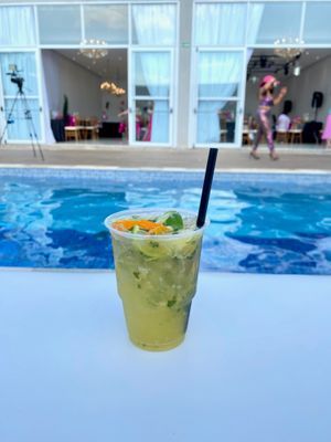 Caipifruta com cachaça, tangerina, abacaxi, limão e hortelã, servida em copo descartável à beira da piscina 