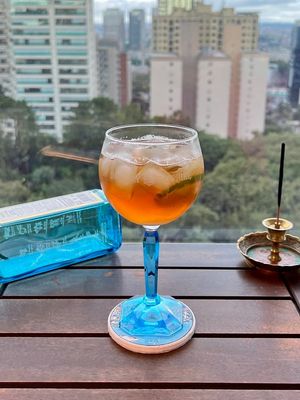 Taça de Gin Tônica com haste azul e garrafa de gin Bombay Sapphire ao fundo